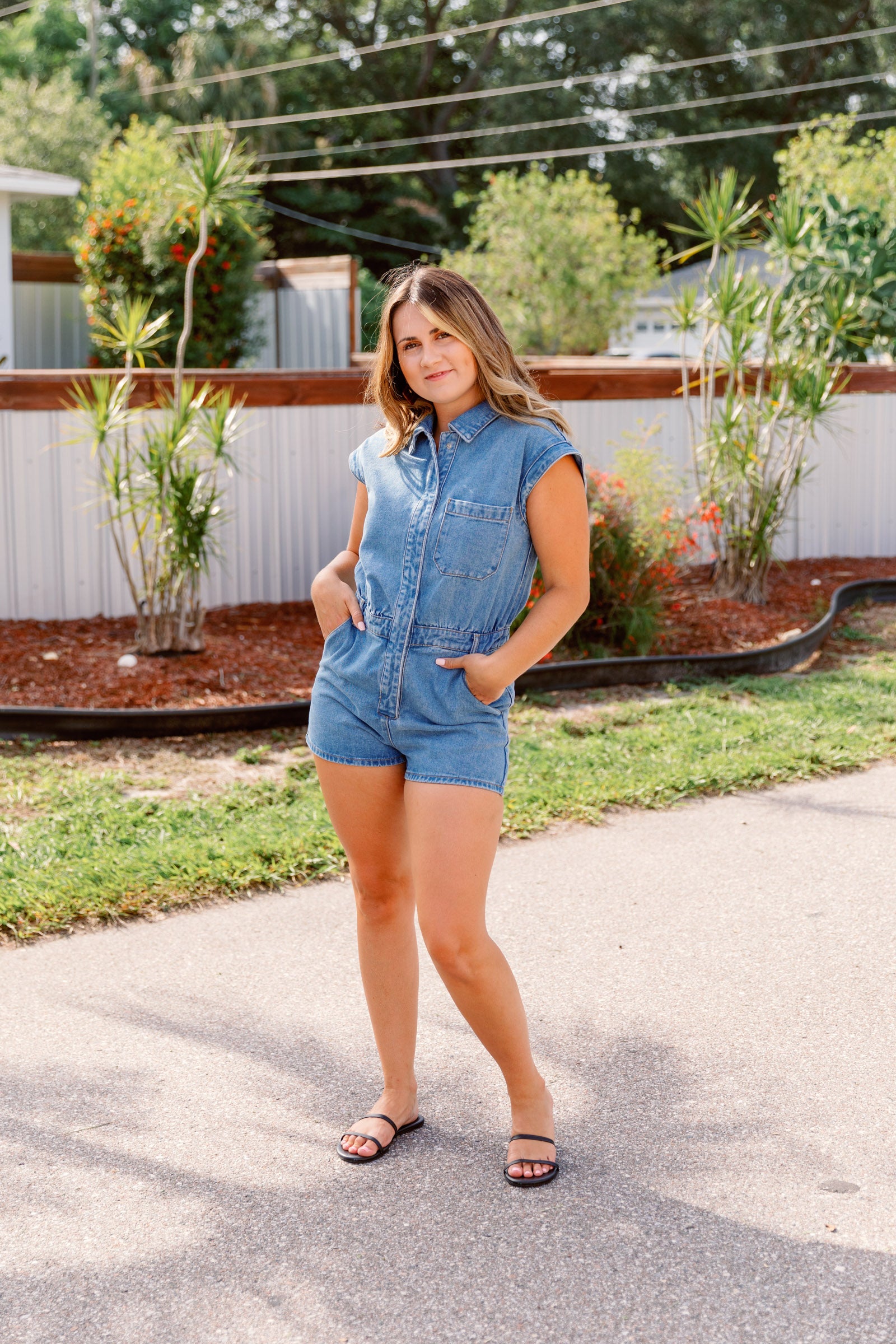 This denim romper has shorts sleeves meeting a collar with buttons all the way down and short slightly fitted shorts. 